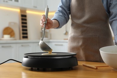 Woman cooking delicious crepe on electrical pancake maker in kitchen, closeup