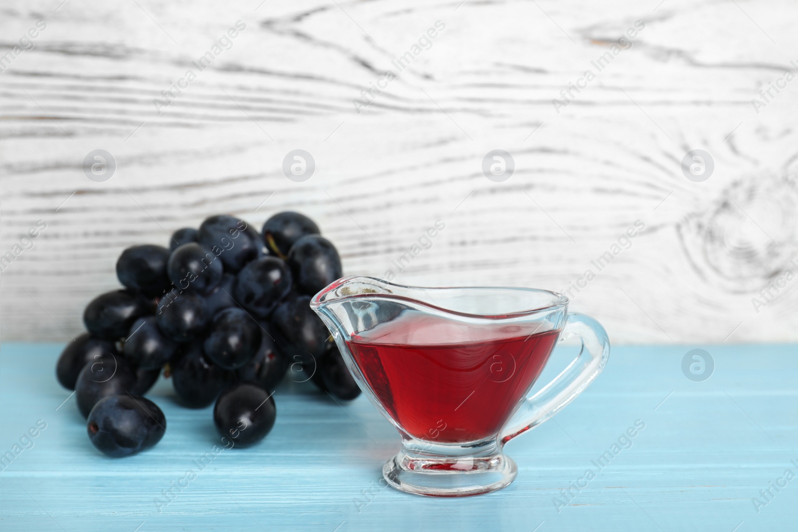 Photo of Glass gravy boat with wine vinegar and fresh grapes on wooden table