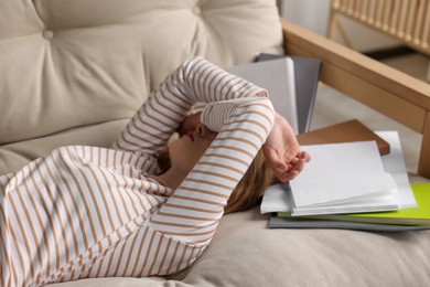 Photo of Young tired woman sleeping near books on couch indoors