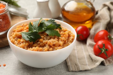 Photo of Delicious red lentils with parsley in bowl and products on light grey table, closeup