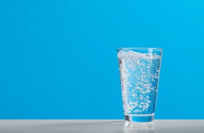 Photo of Glass of soda water on light blue background, space for text