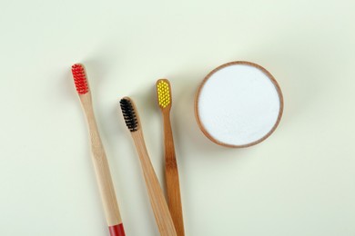 Photo of Bamboo toothbrushes and bowl of baking soda on beige background, flat lay