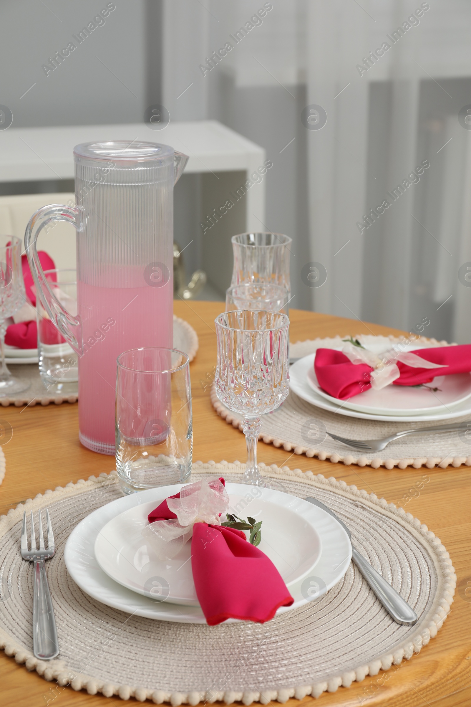 Photo of Color accent table setting. Glasses, plates, jug of beverage and pink napkins in dining room