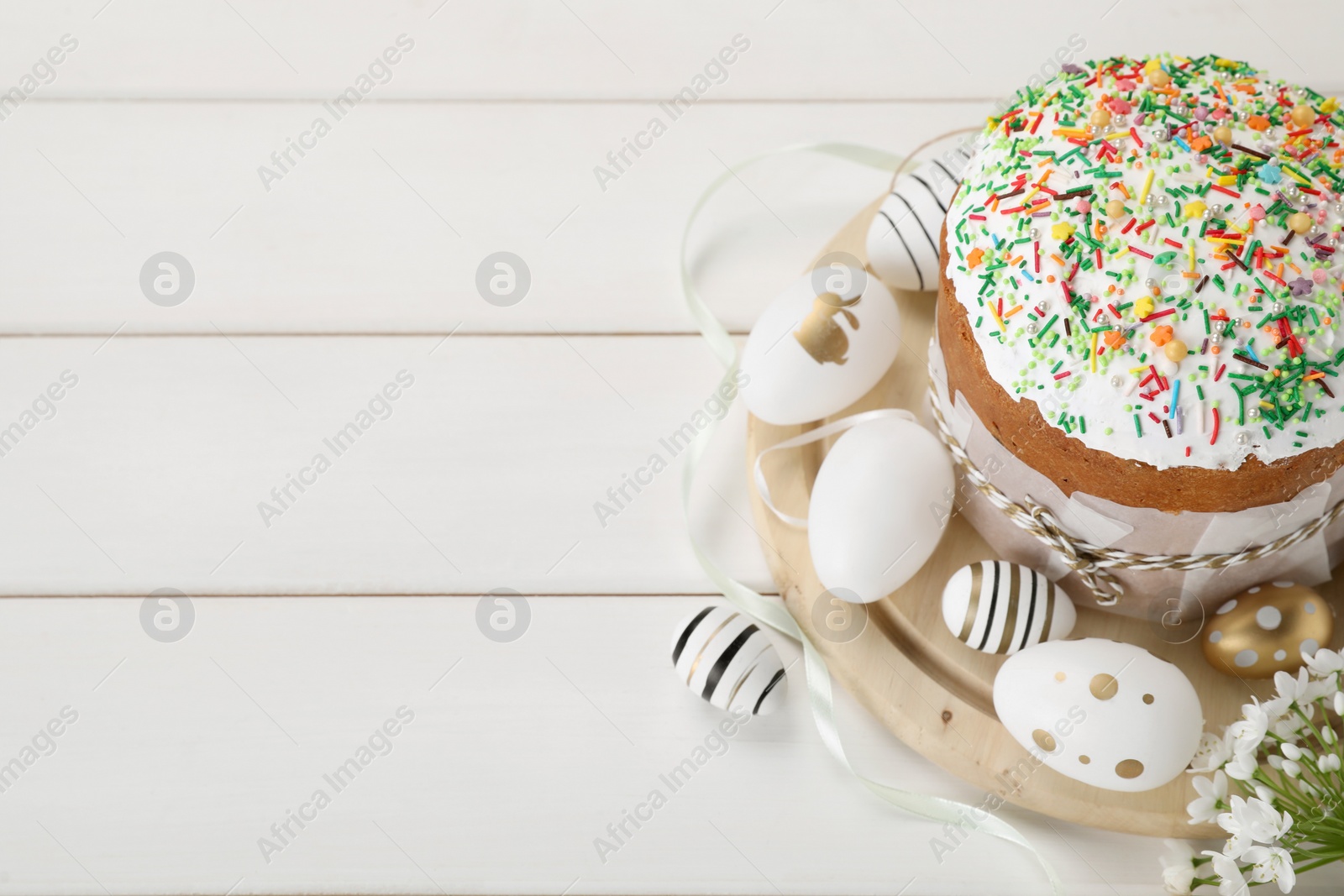 Photo of Traditional Easter cake with sprinkles and painted eggs on white wooden table, space for text