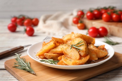 Photo of Plate with tasty baked potatoes and rosemary on wooden board