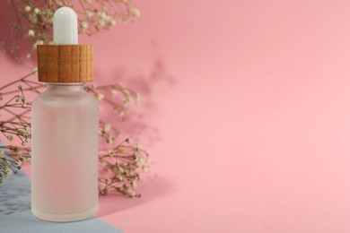 Photo of Bottle of face serum and beautiful flowers on color background, closeup. Space for text