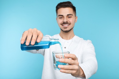 Photo of Young man pouring mouthwash from bottle into glass on color background. Teeth and oral care