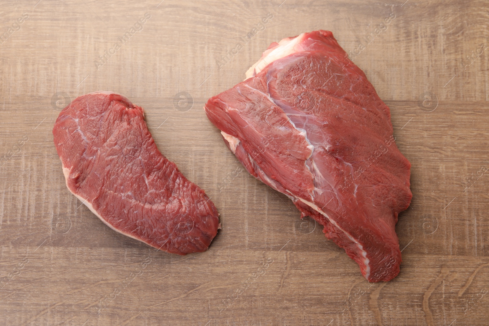 Photo of Pieces of raw beef meat on wooden table, flat lay