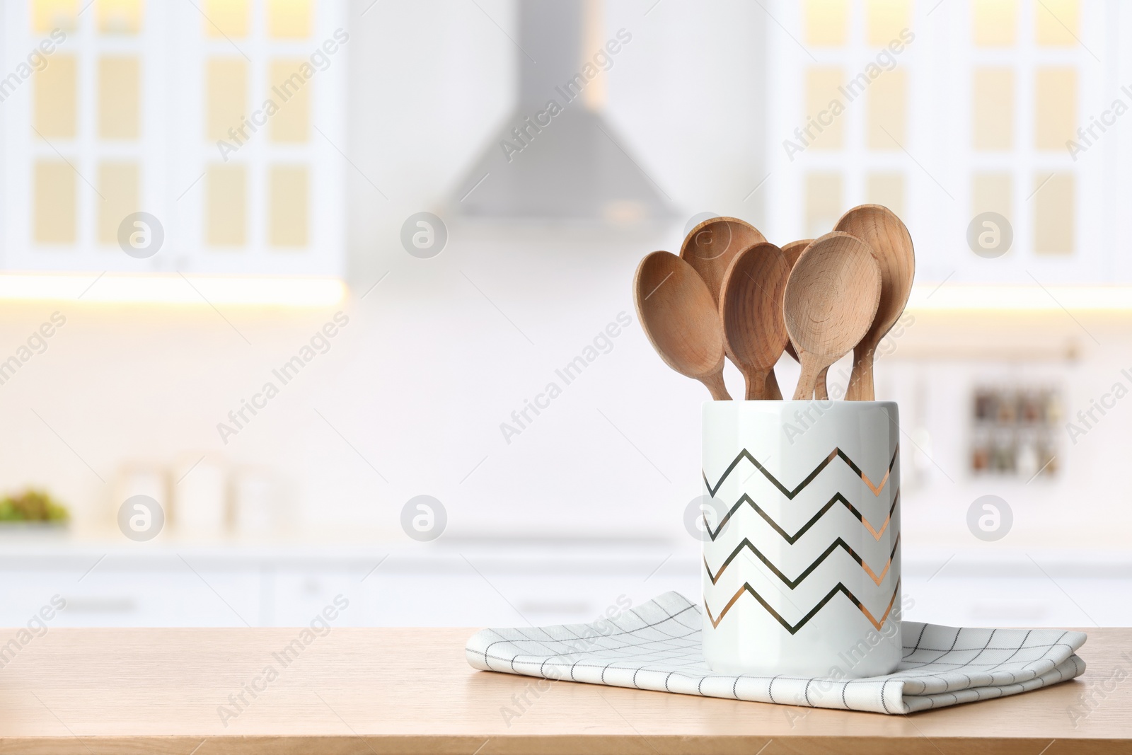 Image of Holder with spoons on wooden table and blurred view of stylish kitchen interior. Mockup for design