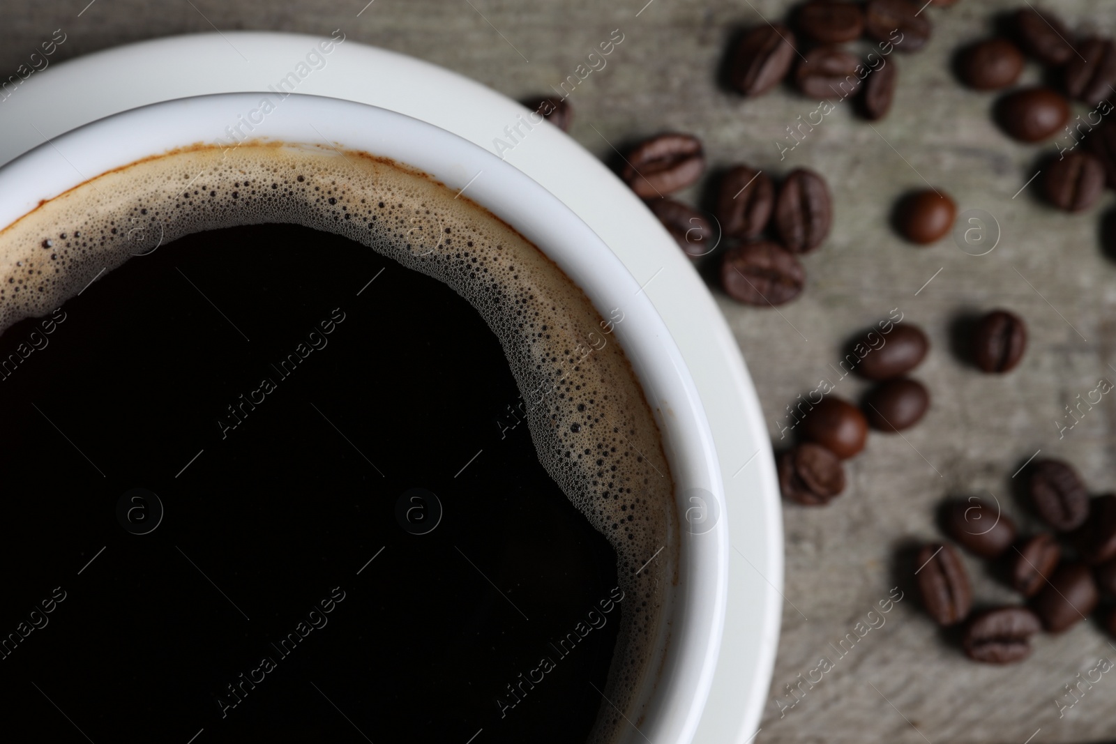 Photo of Cup of hot aromatic coffee and roasted beans on wooden table, top view. Space for text