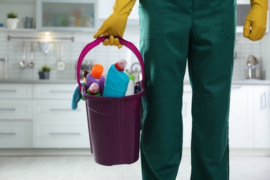 Photo of Janitor with bucket of detergents in kitchen, closeup. Cleaning service