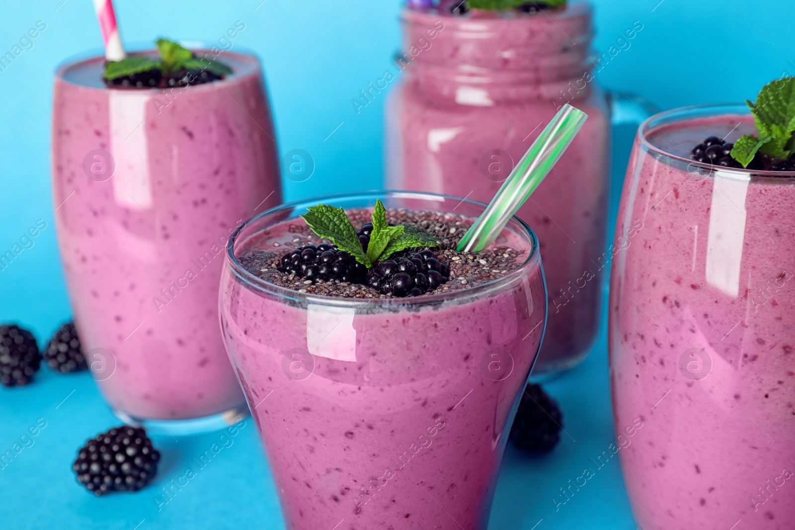 Photo of Glasses with tasty blackberry smoothie on blue background, closeup