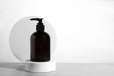 Photo of Bottle of cosmetic product and podiums on light grey table against white background, space for text