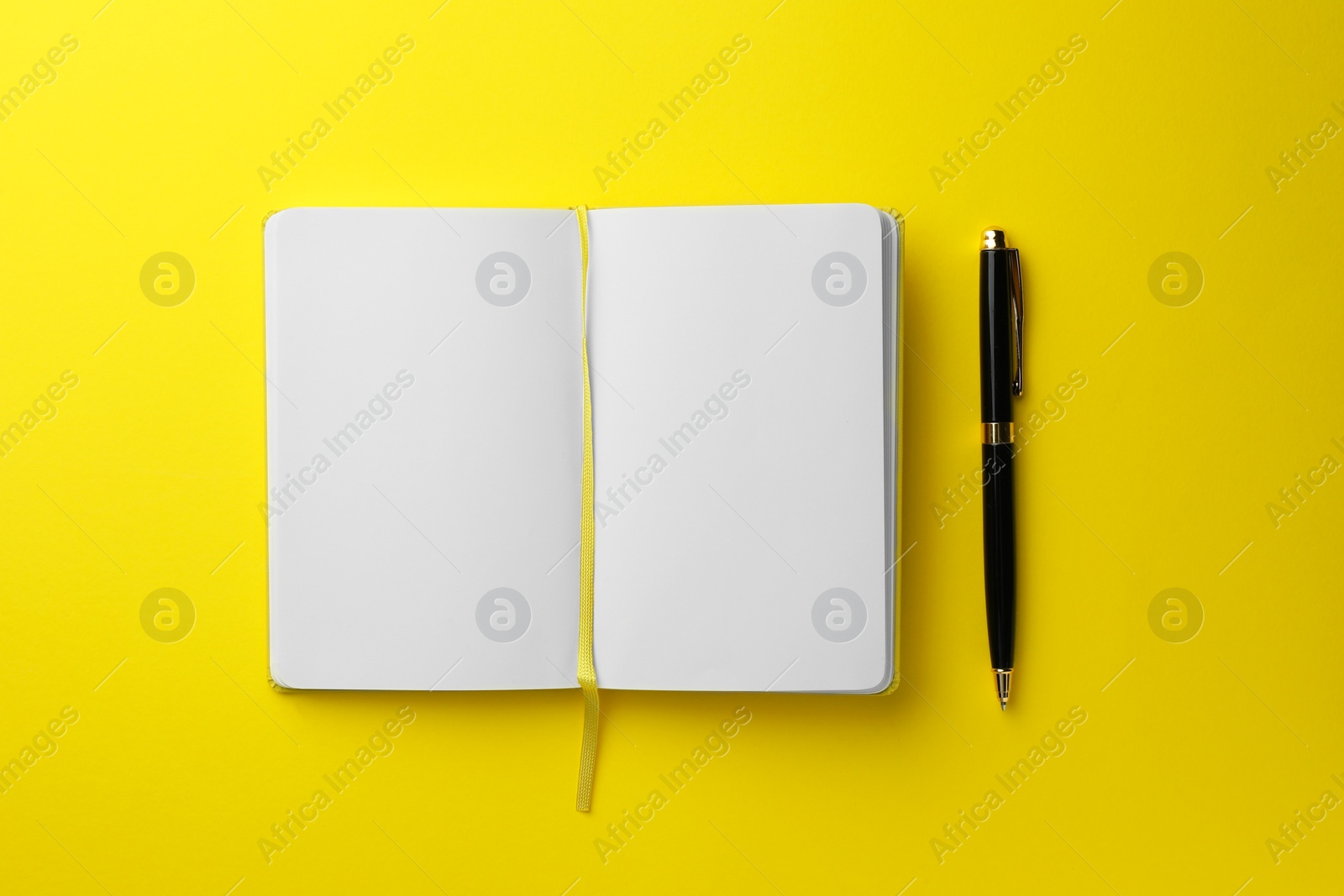 Photo of Open notebook with blank pages and pen on yellow background, top view. Space for text