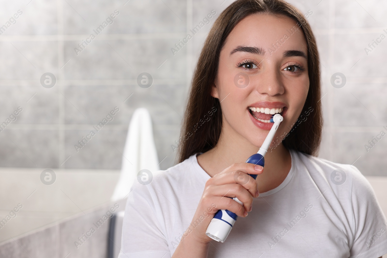 Photo of Young woman brushing her teeth with electric toothbrush in bathroom