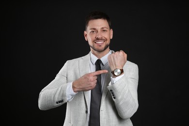 Photo of Happy businessman pointing on wristwatch against black background. Time management