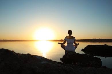 Photo of Woman practicing yoga near river on sunset. Healing concept