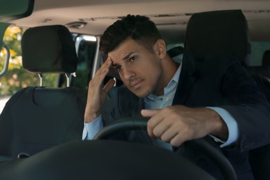 Photo of Stressed man in driver's seat of modern car, view through windshield