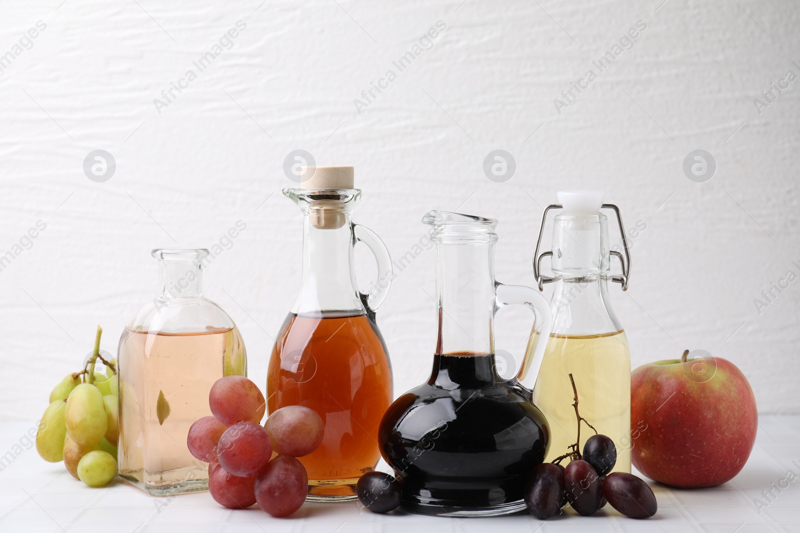 Photo of Different types of vinegar and ingredients on light tiled table, closeup