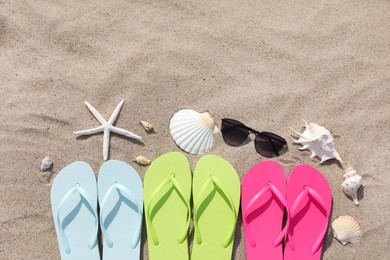 Stylish colorful flip flops, sunglasses, seashells and starfish on sand outdoors, flat lay. Space for text