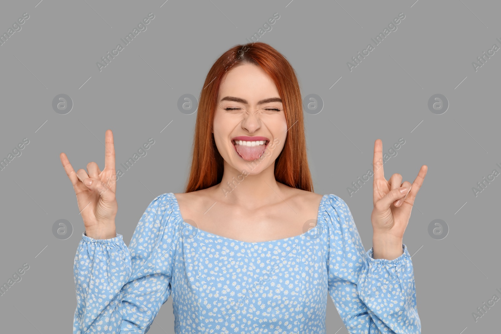 Photo of Happy woman showing her tongue and rock gesture on gray background