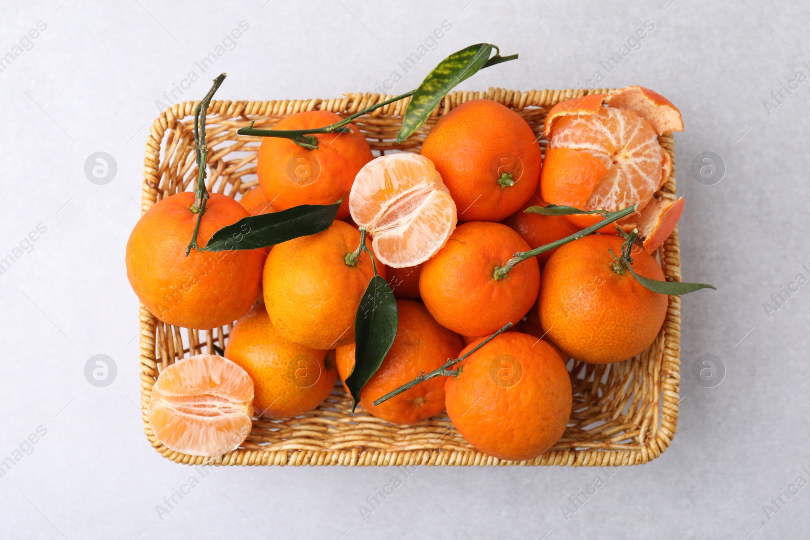 Photo of Fresh ripe tangerines with green leaves in wicker basket on white table, top view