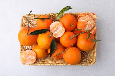 Fresh ripe tangerines with green leaves in wicker basket on white table, top view