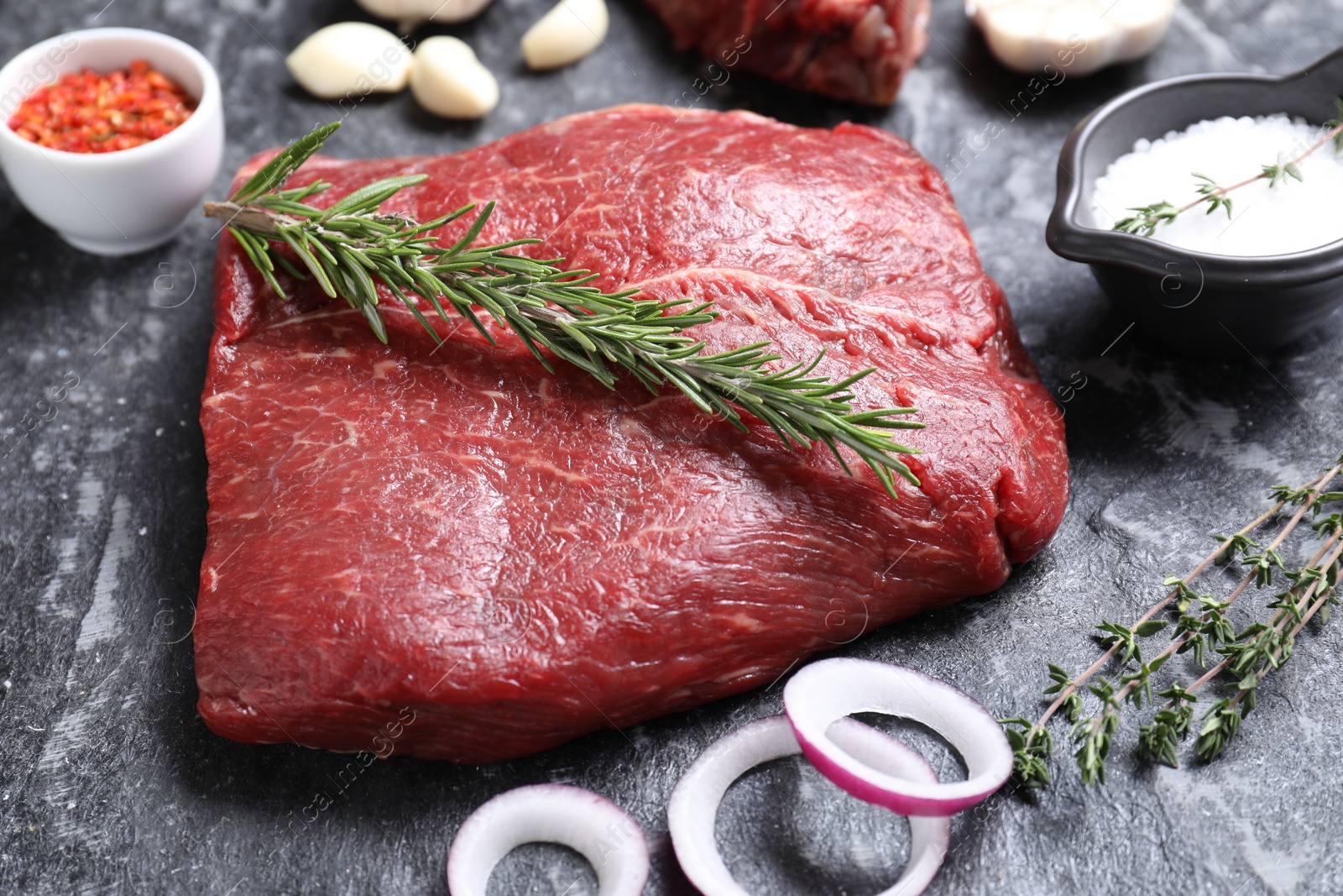 Photo of Fresh raw beef cut and different spices on grey textured table, closeup