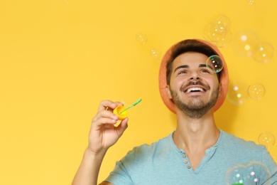 Young man blowing soap bubbles on color background. Space for text