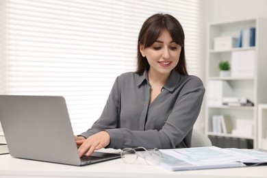 Smiling secretary working with laptop at table in office