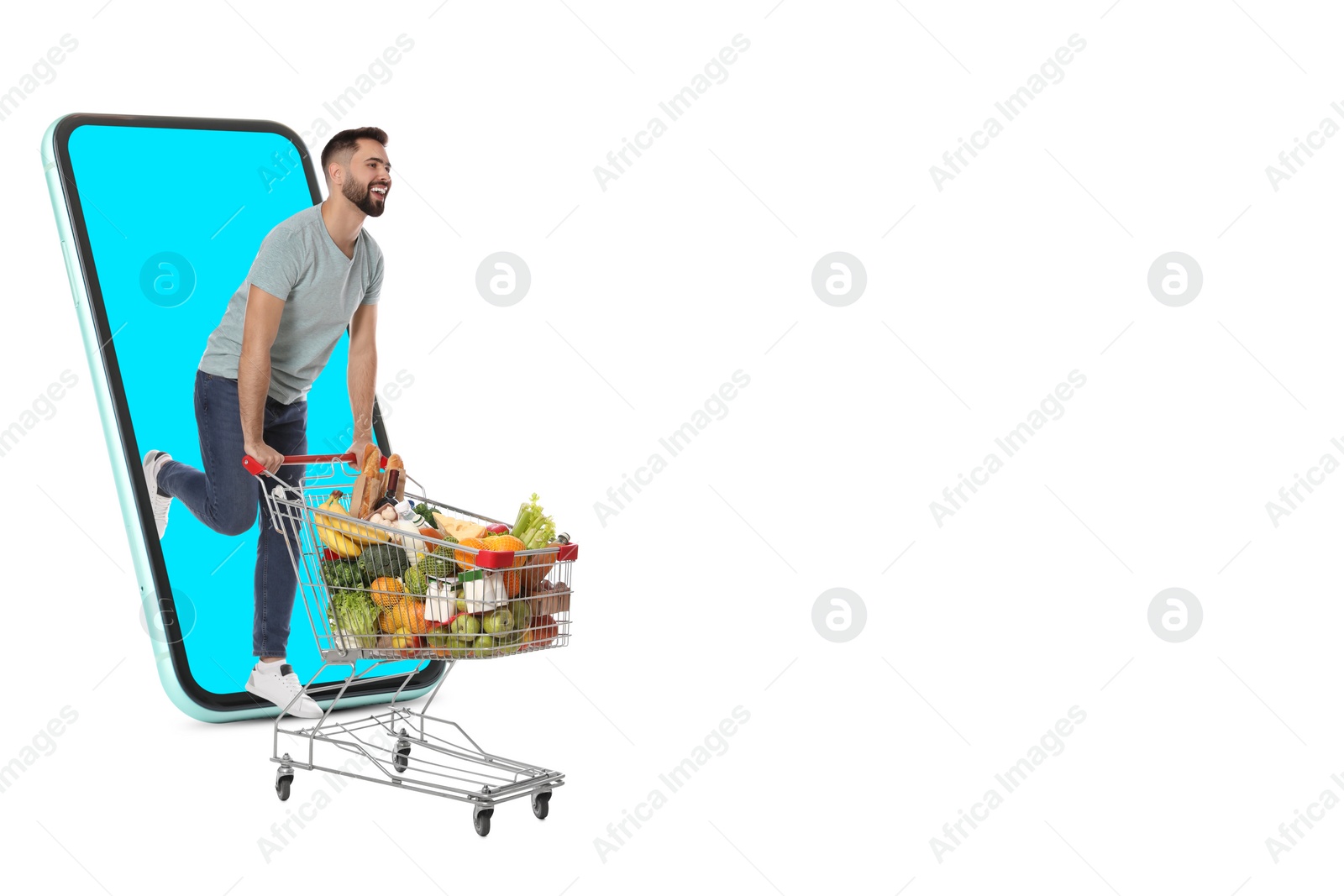 Image of Grocery shopping via internet. Happy man with shopping cart full of products running out of huge smartphone on white background