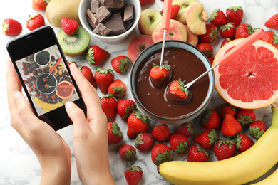 Blogger taking picture of chocolate fondue and fruits at table, top view