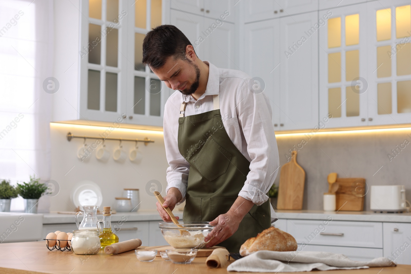 Photo of Making bread. Man preparing dough in bowl at wooden table in kitchen