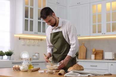 Making bread. Man preparing dough in bowl at wooden table in kitchen