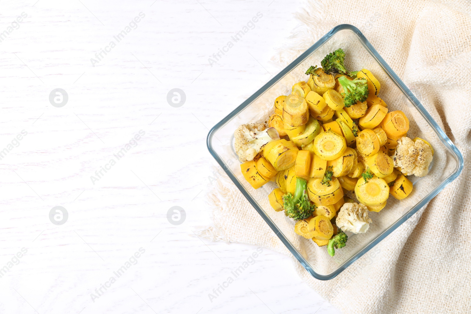 Photo of Baked yellow carrot with broccoli and cauliflowers in glass dish on white wooden table, flat lay. Space for text