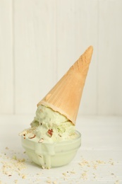 Delicious pistachio ice cream with chopped nuts in wafer cone on white wooden table