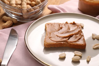Photo of Toast with tasty nut butter, peanuts and knife on table, closeup