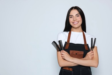 Photo of Portrait of happy hairdresser with professional combs on light background, space for text