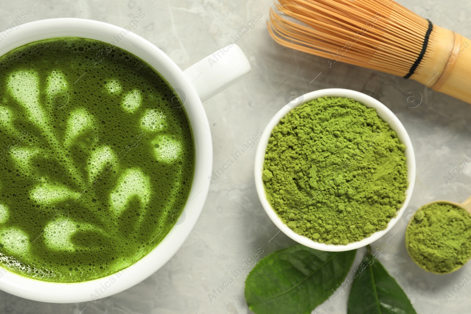 Photo of Delicious matcha latte, powder, leaves and whisk on grey textured table, flat lay