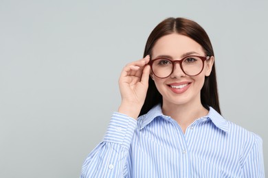 Portrait of smiling woman in stylish eyeglasses on grey background. Space for text