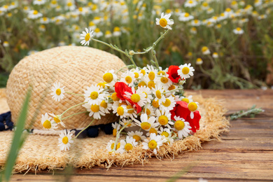 Photo of Bouquet of poppies and chamomiles with straw hat on wooden table outdoors