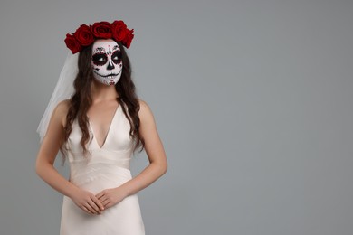 Photo of Young woman in scary bride costume with sugar skull makeup and flower crown on light grey background, space for text. Halloween celebration