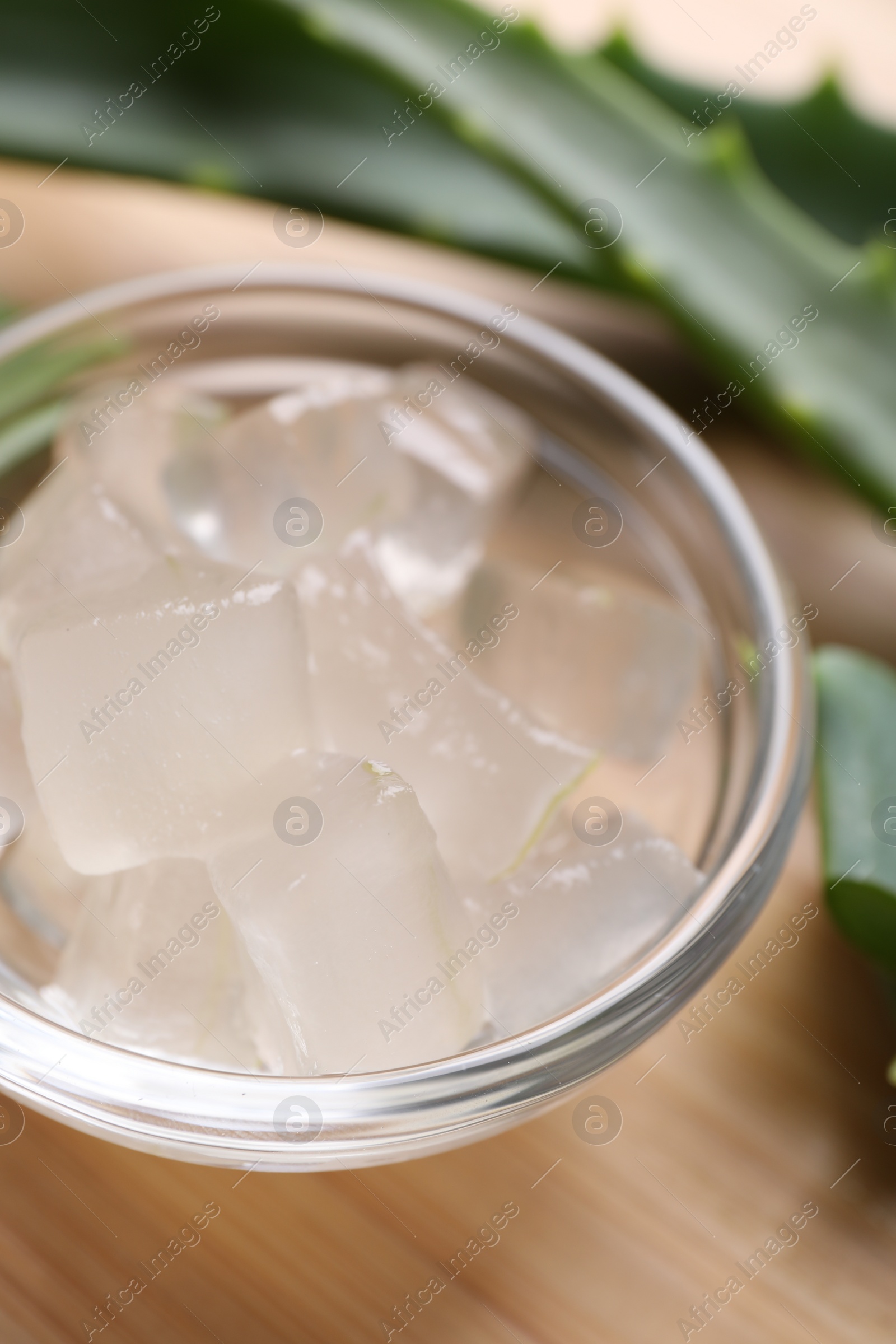 Photo of Aloe vera gel and slices of plant on wooden table, closeup