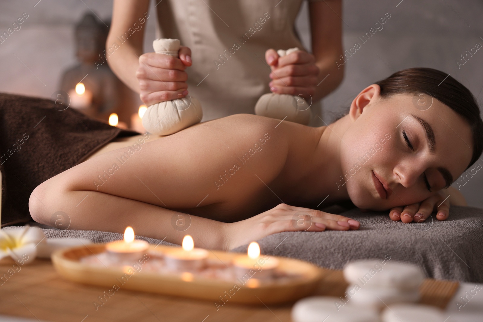 Photo of Spa therapy. Beautiful young woman lying on table during herbal bag massage in salon