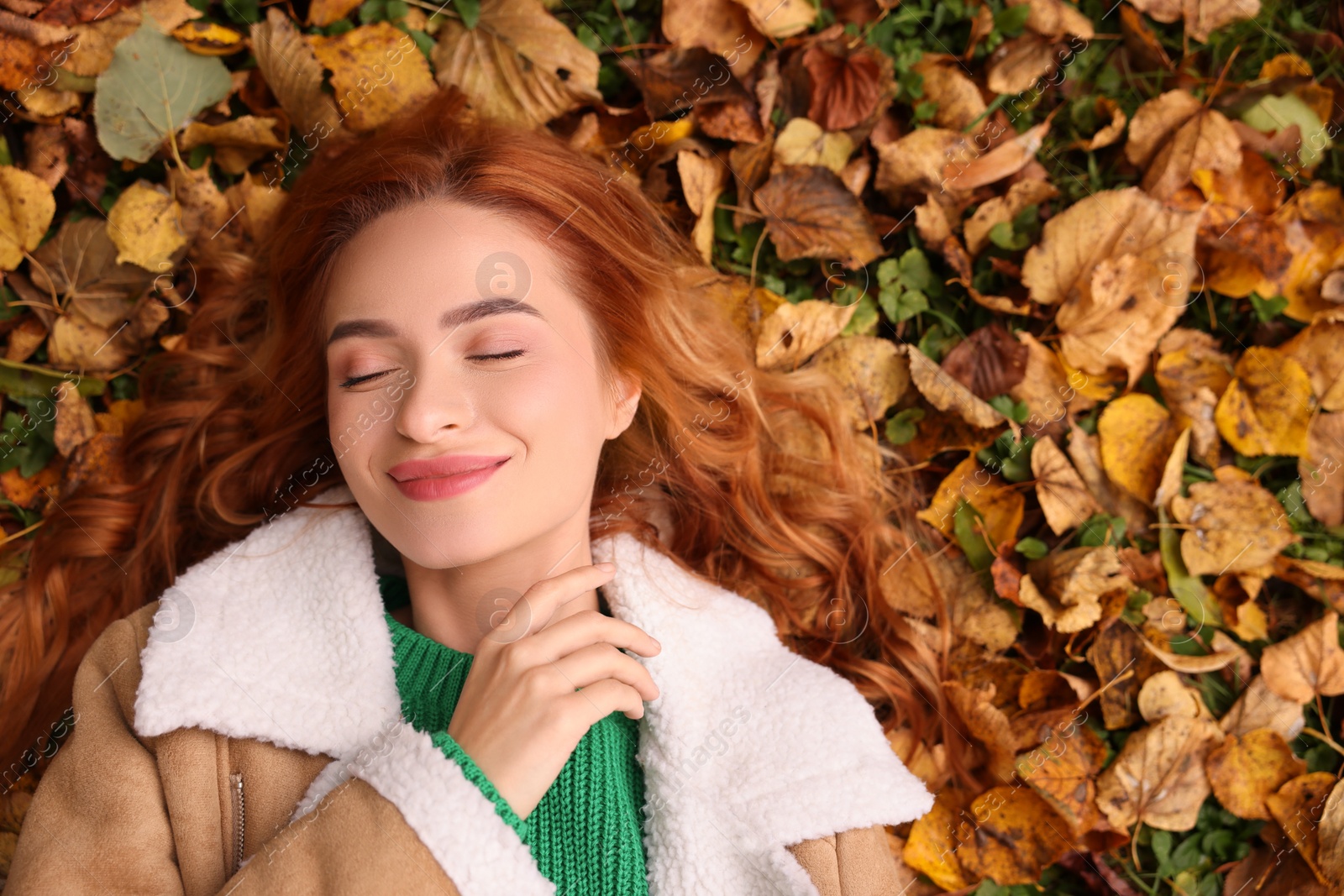 Photo of Beautiful woman lying among autumn leaves outdoors, top view. Space for text