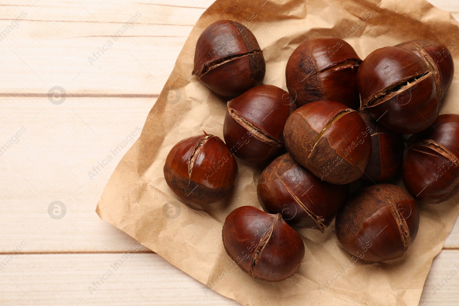 Photo of Roasted edible sweet chestnuts on wooden table, flat lay. Space for text