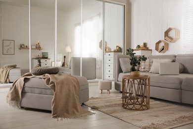 Photo of Comfortable grey sofa, ottoman and wardrobe with mirror doors in living room interior