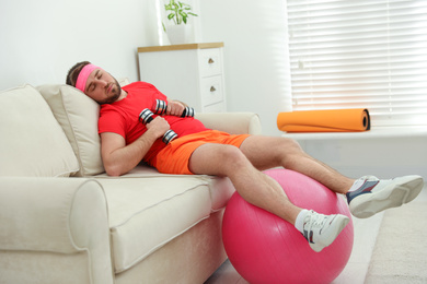 Photo of Lazy young man with sport equipment on sofa at home