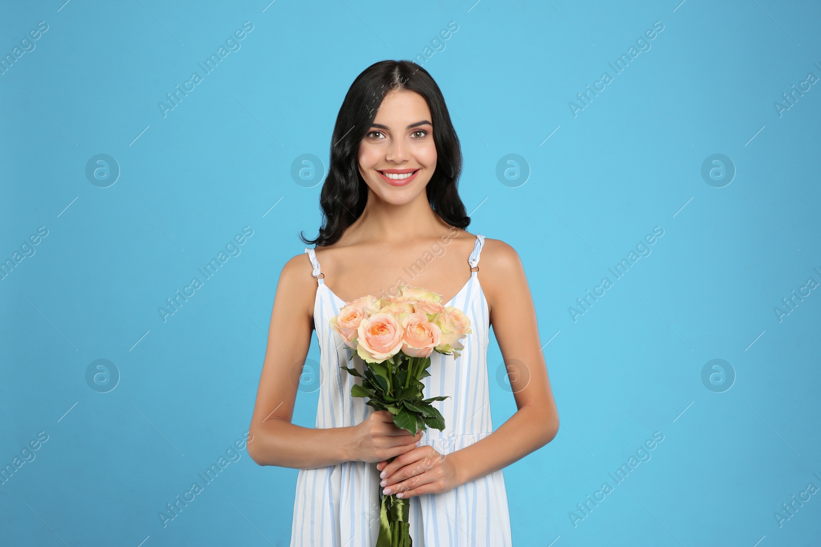 Photo of Portrait of smiling woman with beautiful bouquet on light blue background