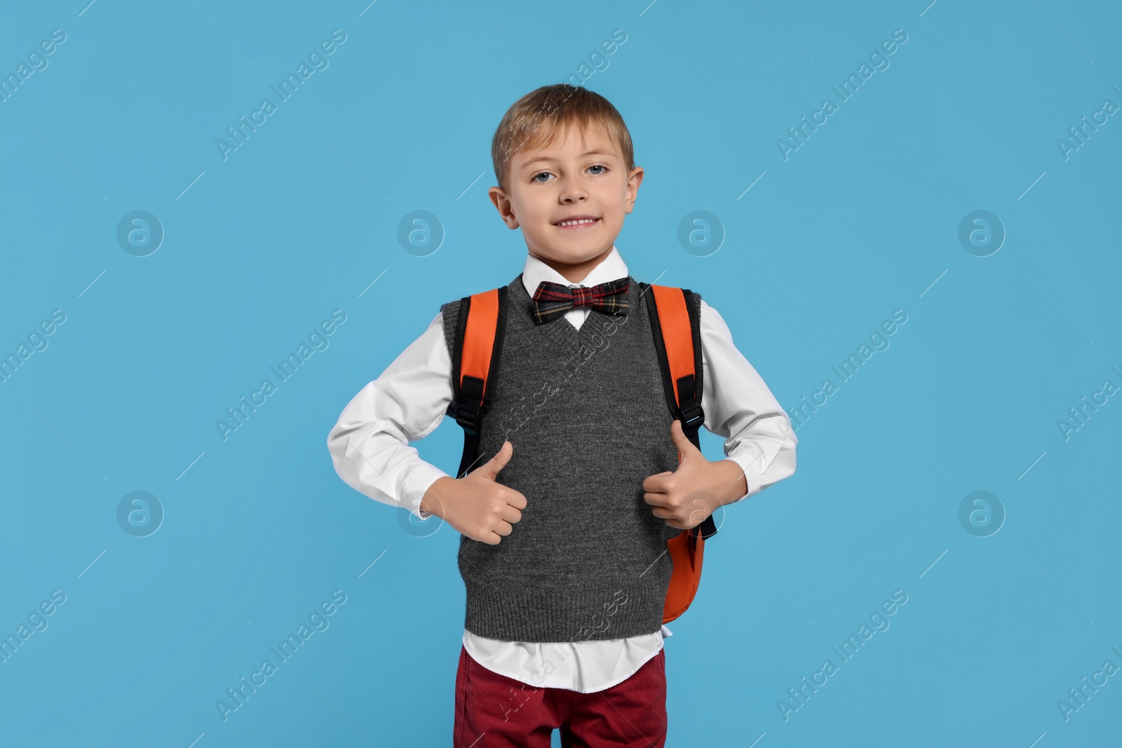 Photo of Happy schoolboy with backpack showing thumbs up gesture on light blue background